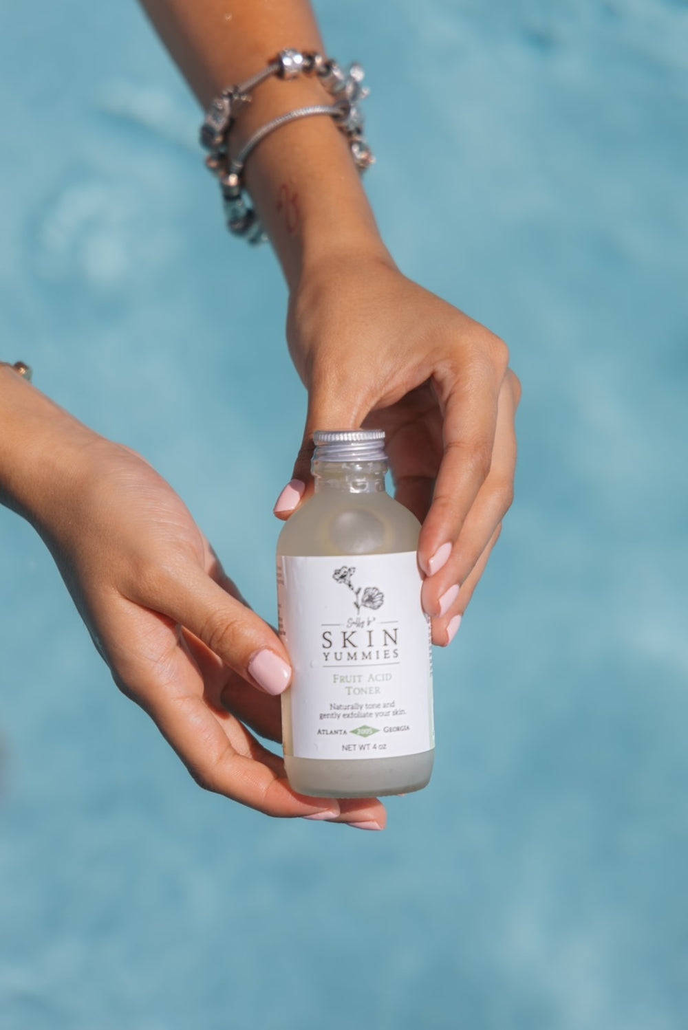 Hands holding a bottle of Fruit Acid Toner over blue pool water